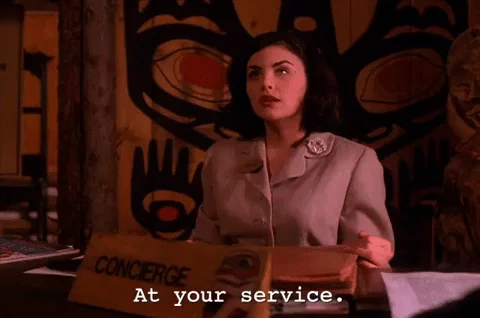 Young woman sitting at a desk in with a Pacific Northwest indiginous banner backdrop awkwardly saying "at your service"