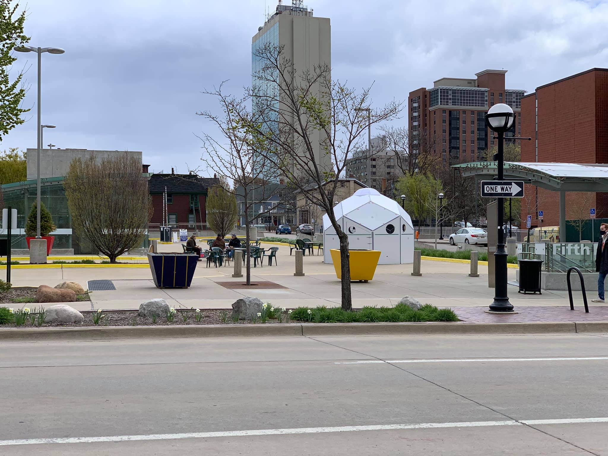 Photo of the Earth Day event at the Center of the City Parking Lot showing a handful of attendees sitting in plastic monobloc chairs surrounded by empty space